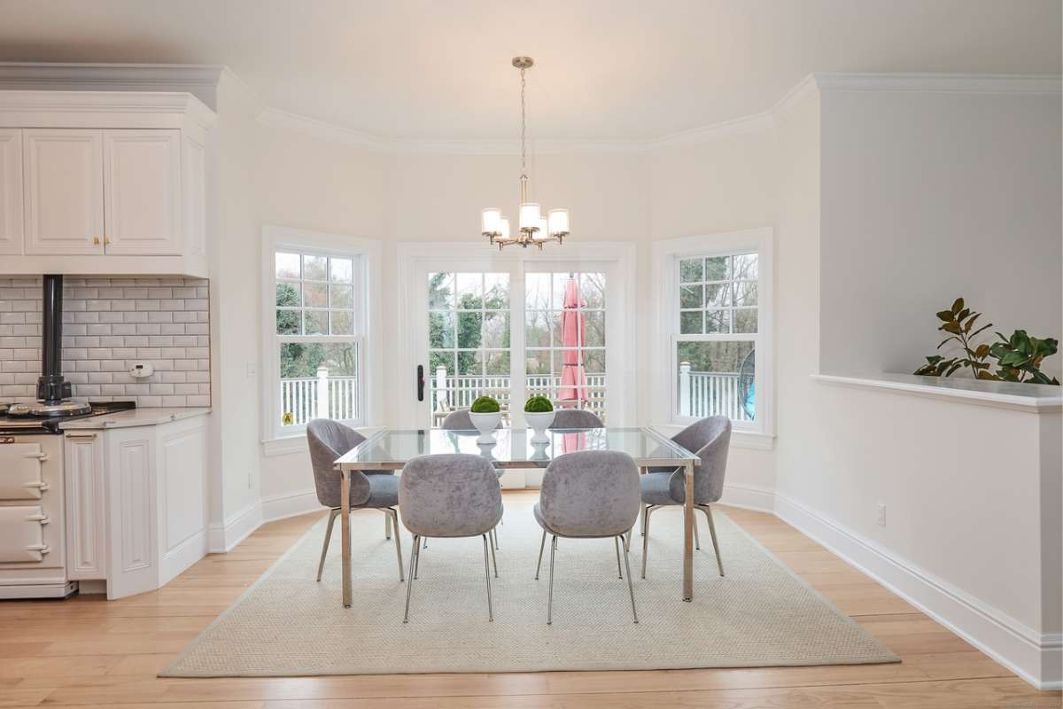 A dining room with a rug, wooden floor, windows, and a dining table surrounded by chairs.