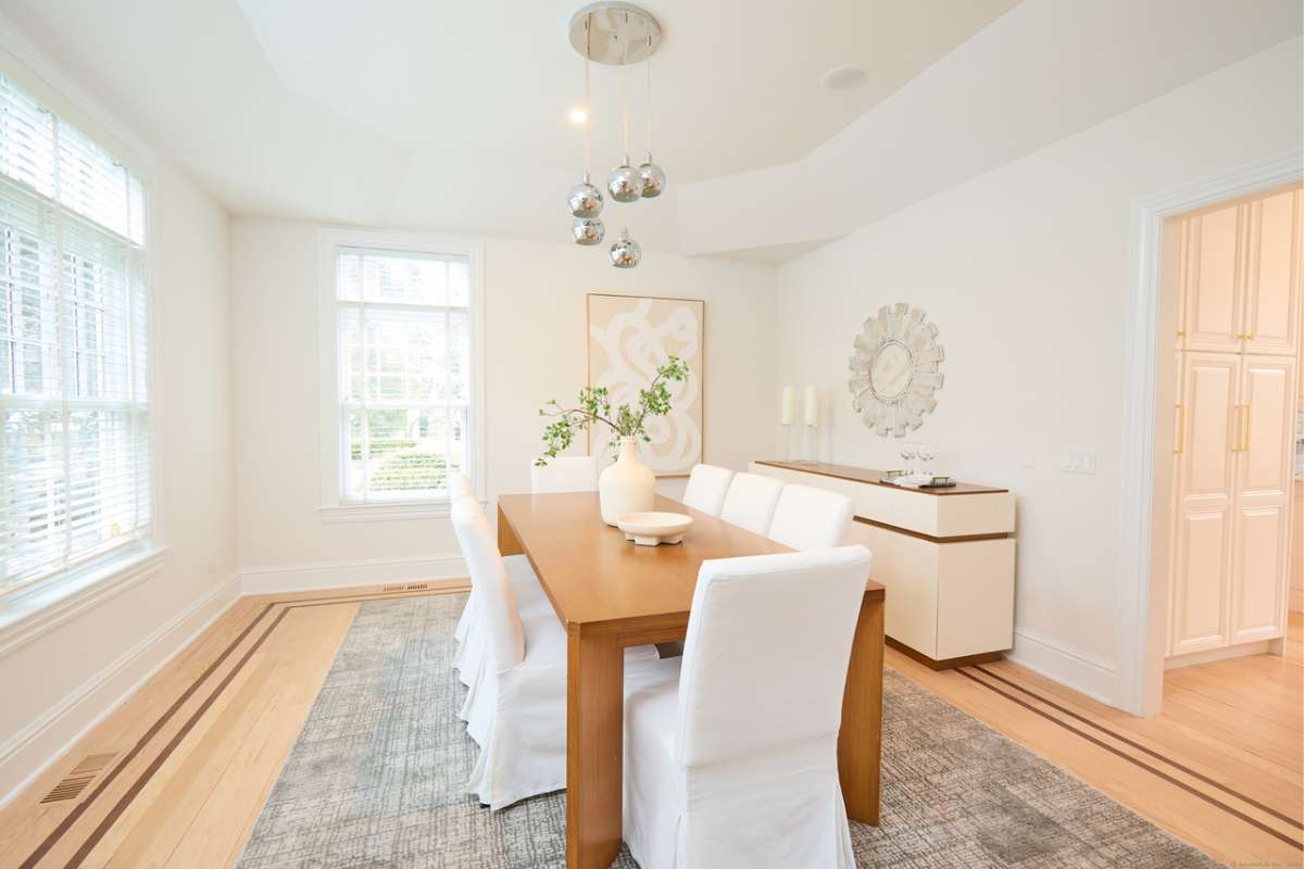 A dining room with a rug, wooden floor, windows, and a dining table surrounded by chairs.
