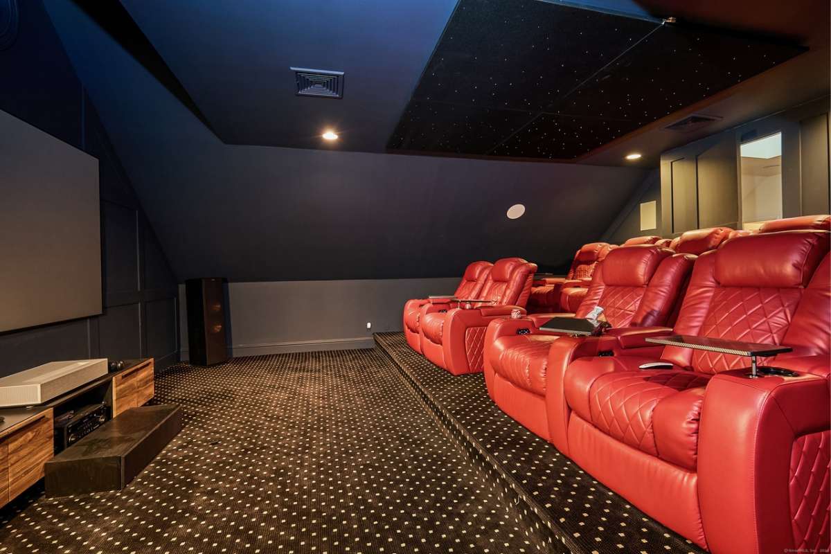A home theater with red chairs, a black floor, a black ceiling, and a large screen.