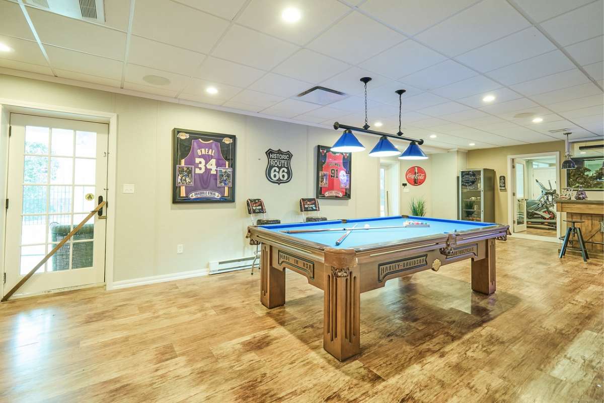 A game room with a wooden floor, lighting, and a pool table.