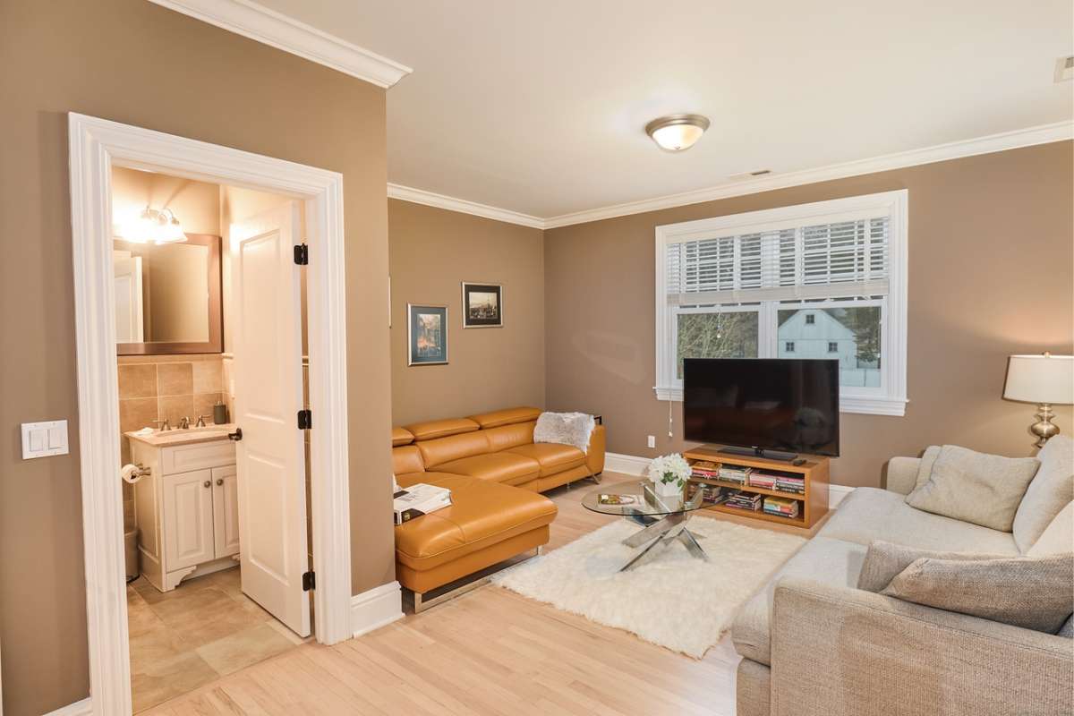 A lounge with a TV, brown couch, center table, window, and white ceiling.