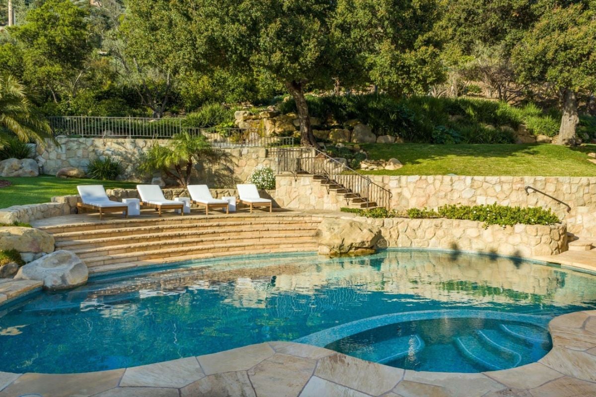 A swimming pool with a jacuzzi, stairs, and chairs.
