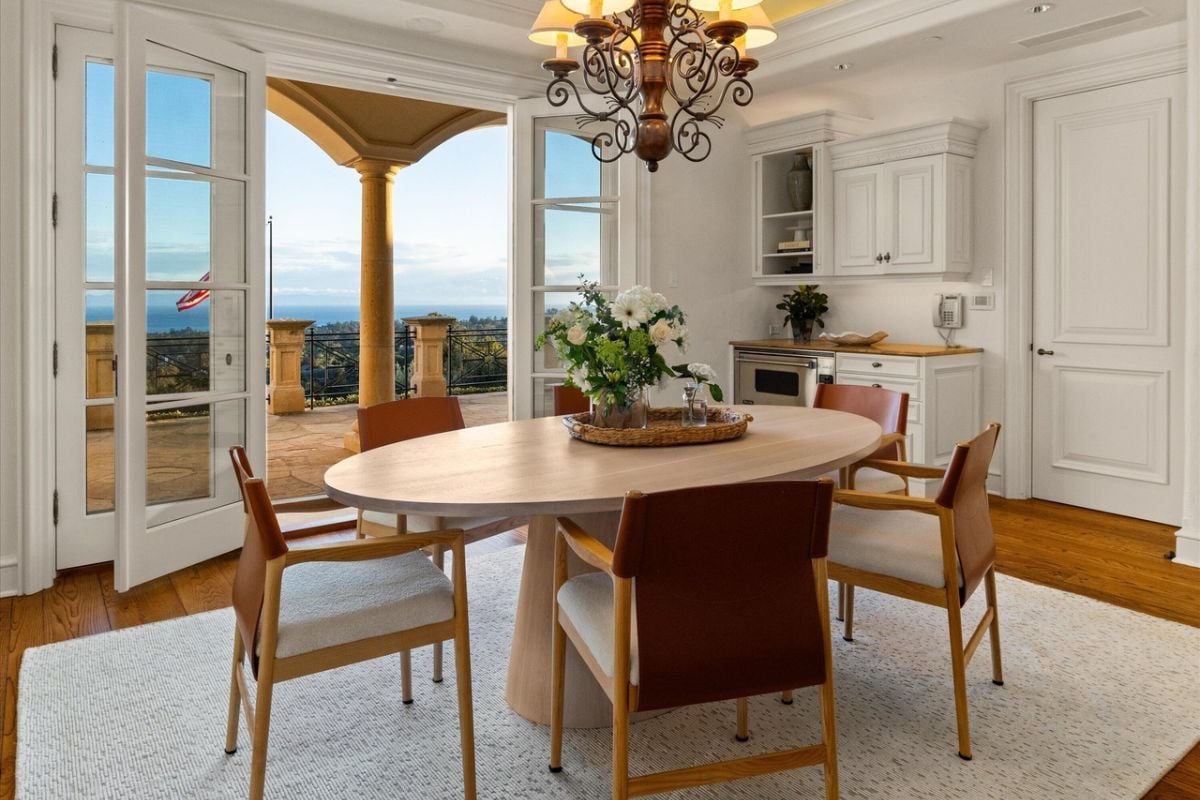 A dining room with a rug, chandelier, and a round dining table surrounded by chairs.