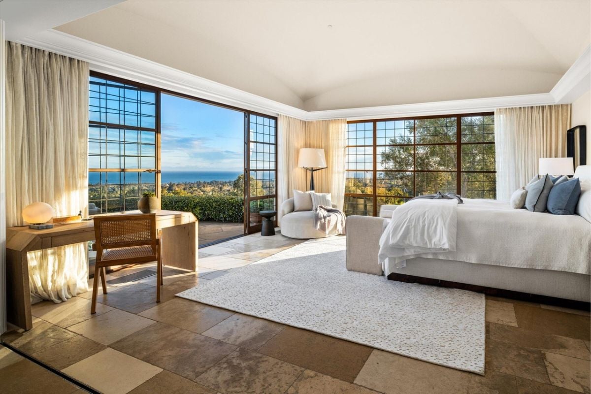 A bedroom with a bed, windows, desk, and chairs.
