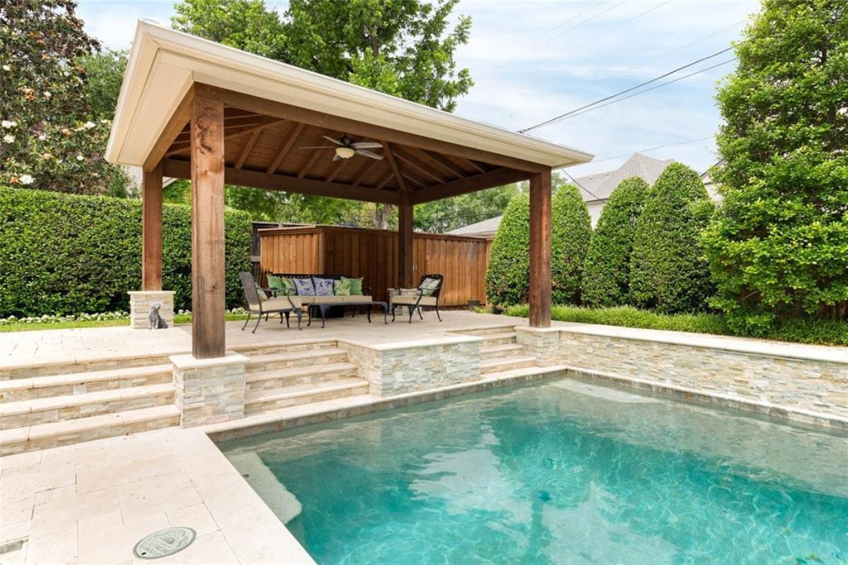 A swimming pool and pergola with a coffee table and chairs.