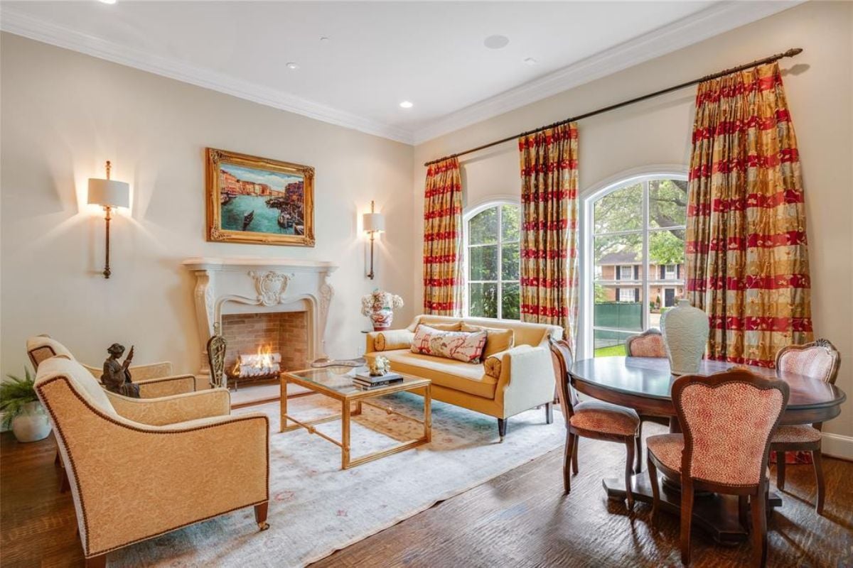 A living room with a fireplace, painting, white ceiling, windows, couches, a center table, and a round table surrounded by chairs.