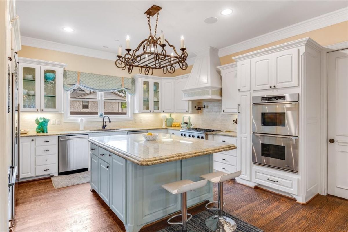 A kitchen with a center island, stools, countertop, sink, chandelier, and kitchen appliances.