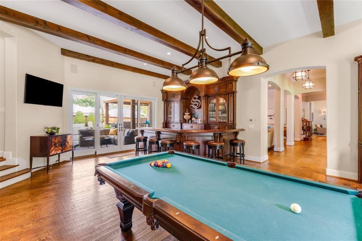 A bar with a vaulted ceiling, countertop, stools, and a pool table.