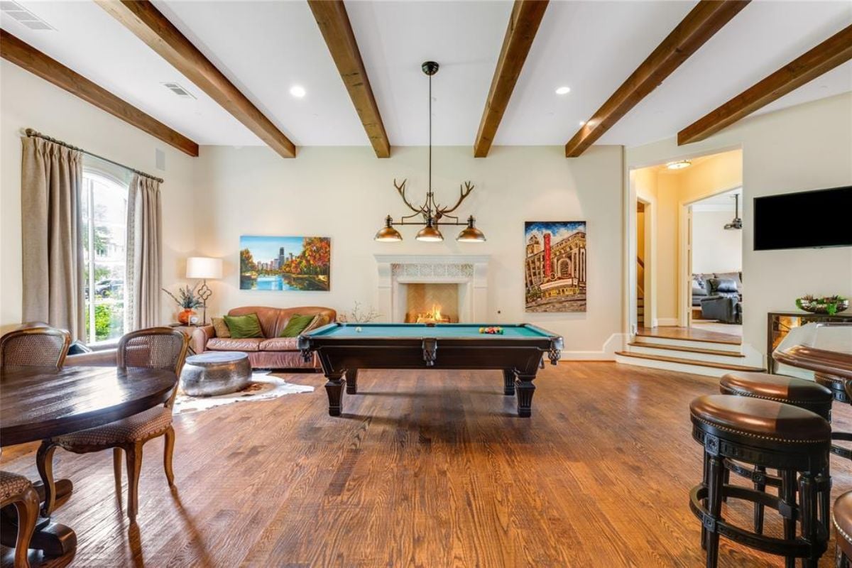 A game room with a vaulted ceiling, fireplace, couch, paintings, and a pool table.
