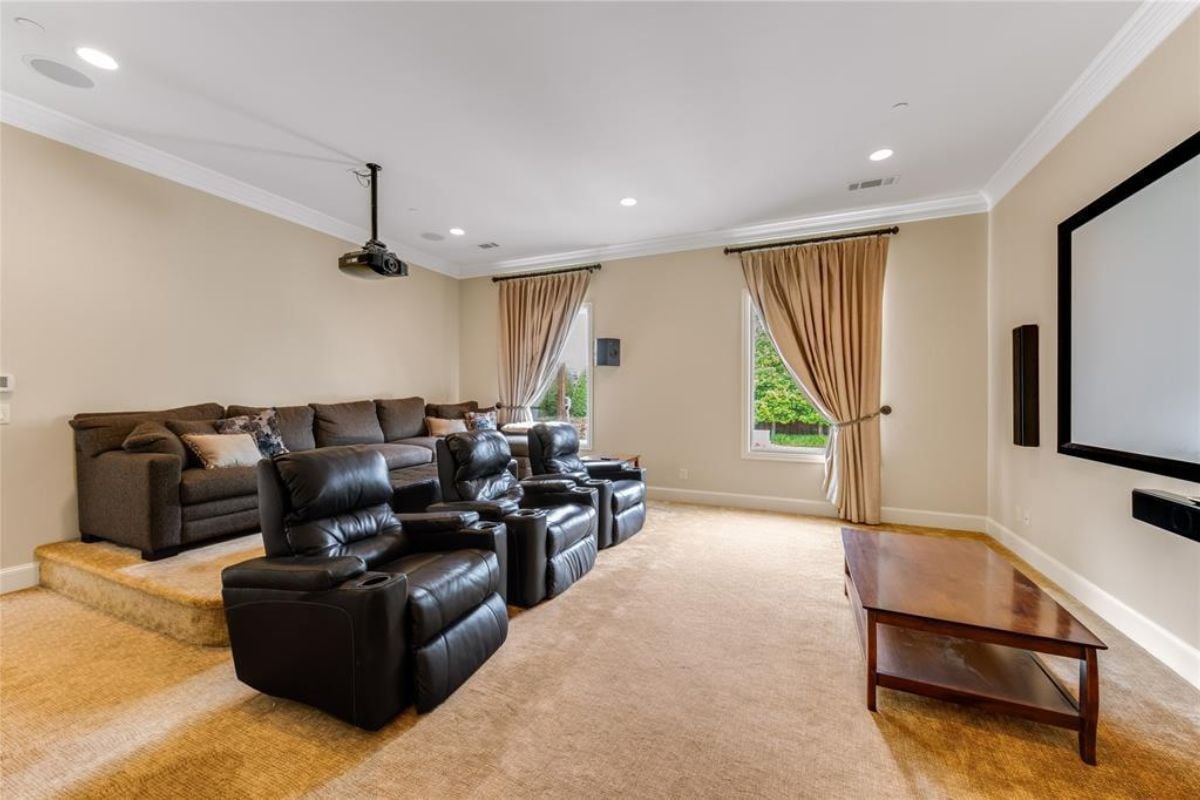 A home theater with windows, black chairs, a table, and a large screen.