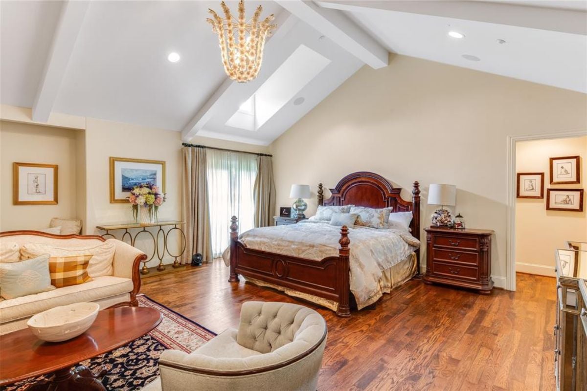 A bedroom with a bed, window, nightstand, wooden floor, vaulted ceiling, chairs, couch, and coffee table.