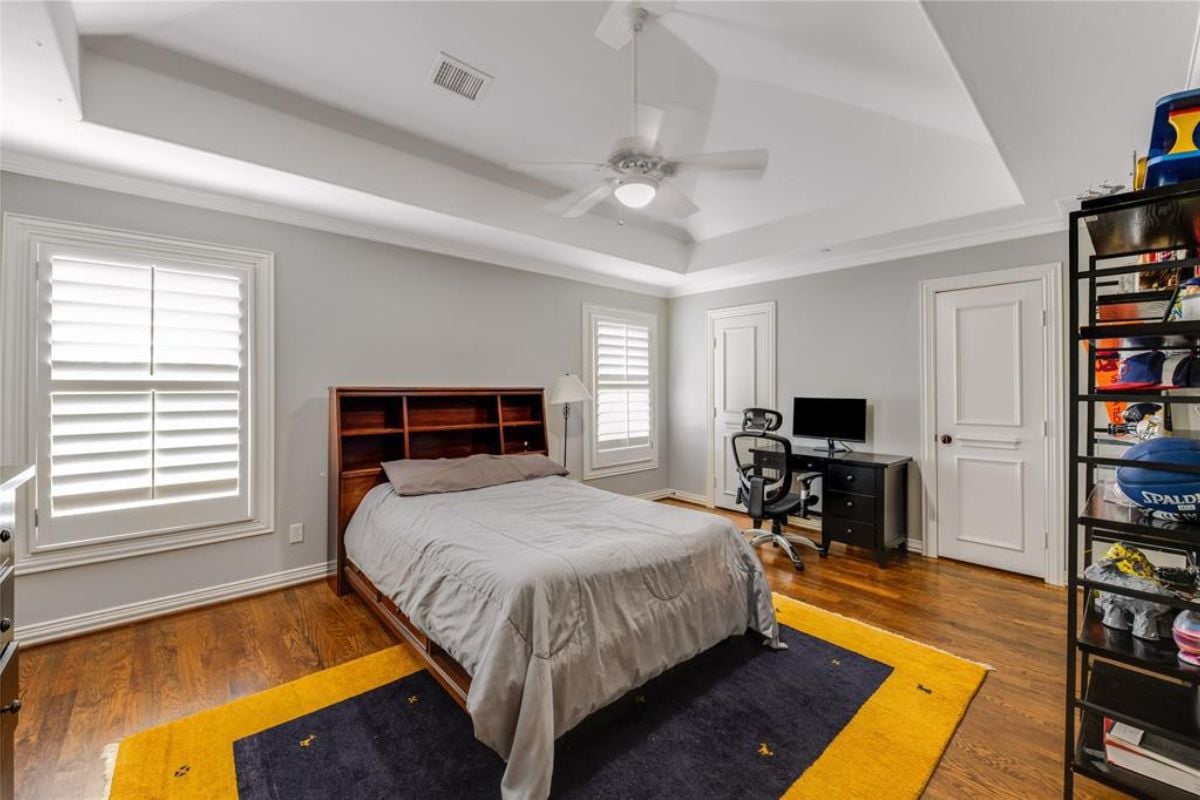 A bedroom with a bed, windows, a rug, a desk, and a chair.