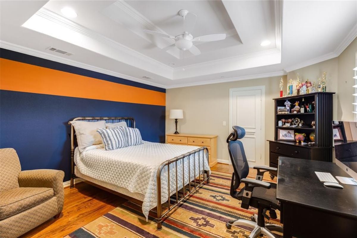 A bedroom with a bed, cabinet, shelf, a rug, desk, and a chair.