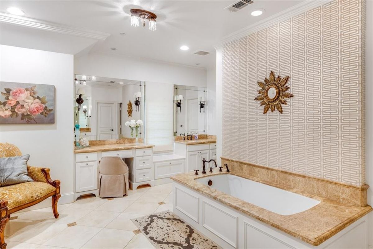 A bathroom with a tiled floor, bathtub, powder area, mirrors, and chairs.