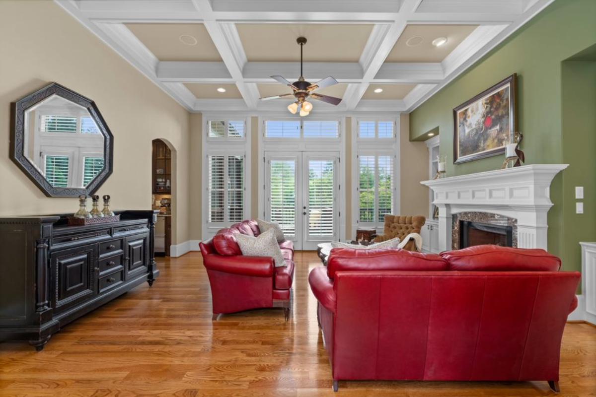 A living room with a fireplace, painting, exposed beam ceiling, ceiling fan, mirror, and red couches.