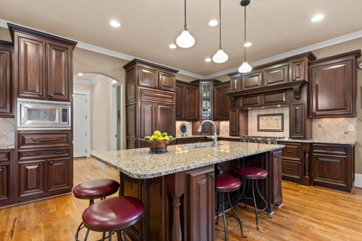 A kitchen with an island, chairs, sink, countertop, cabinets, and kitchen appliances.