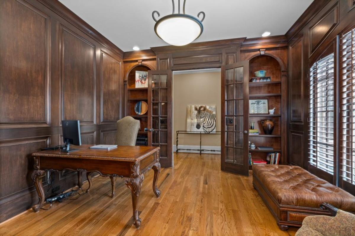 A home office with a couch, shelves, window, chandelier, desk, and chair.