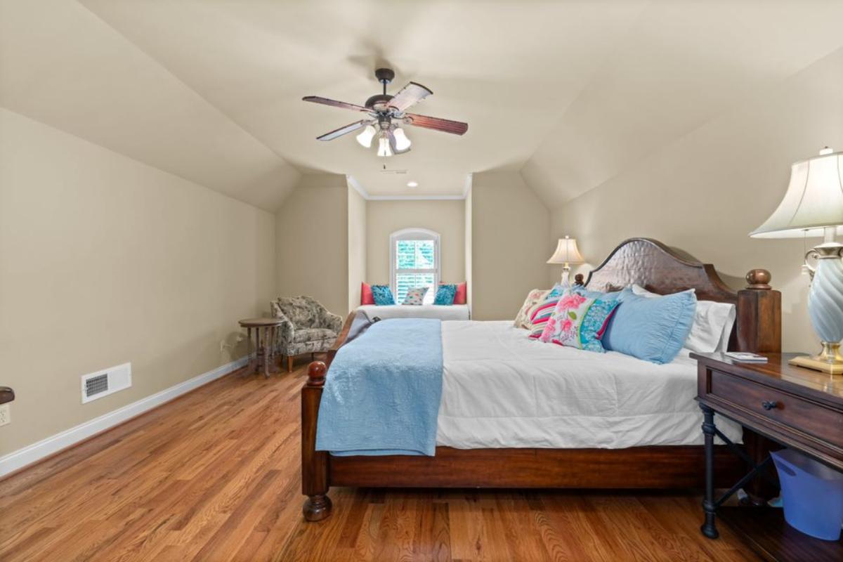 A bedroom with a bed, ceiling fan, side table, studio couch, and bench seating.