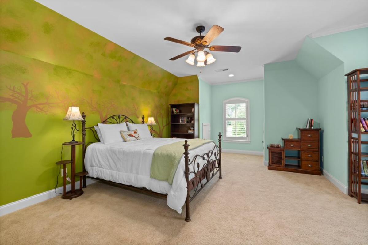 A bedroom with a bed, painted walls, nightstand, ceiling fan, and cabinets.