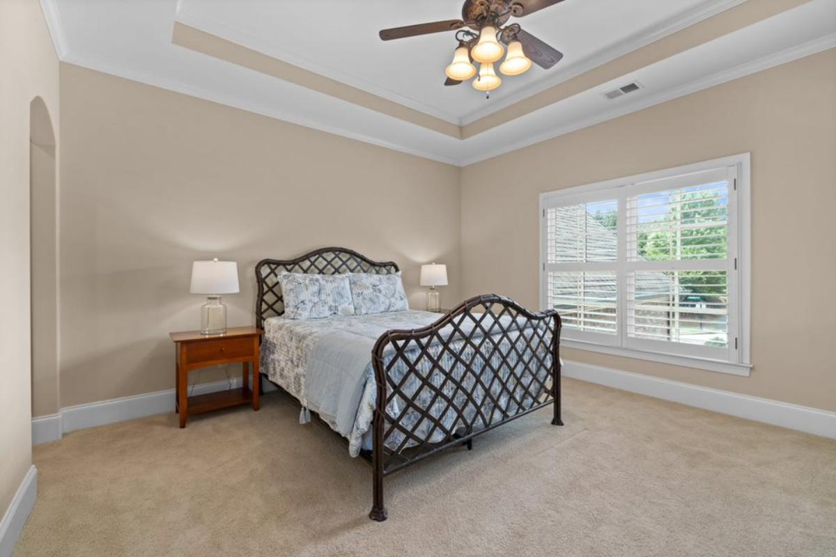 A bedroom with a bed, side table, ceiling fan, and window.