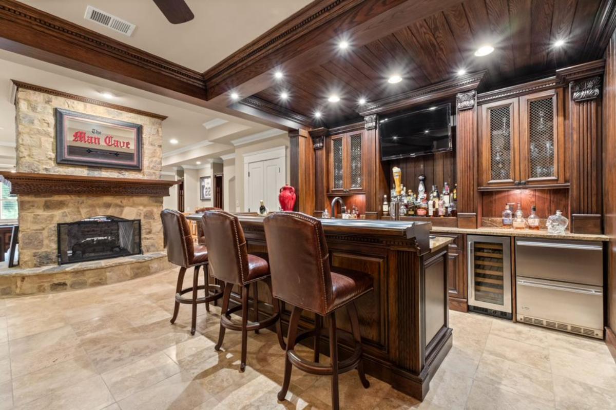 A bar with a stone fireplace, countertop, stools, and cabinets.