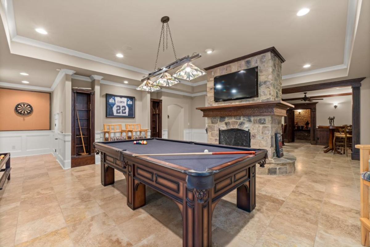 A game room with a TV, stone fireplace, tiled floor, and pool table.