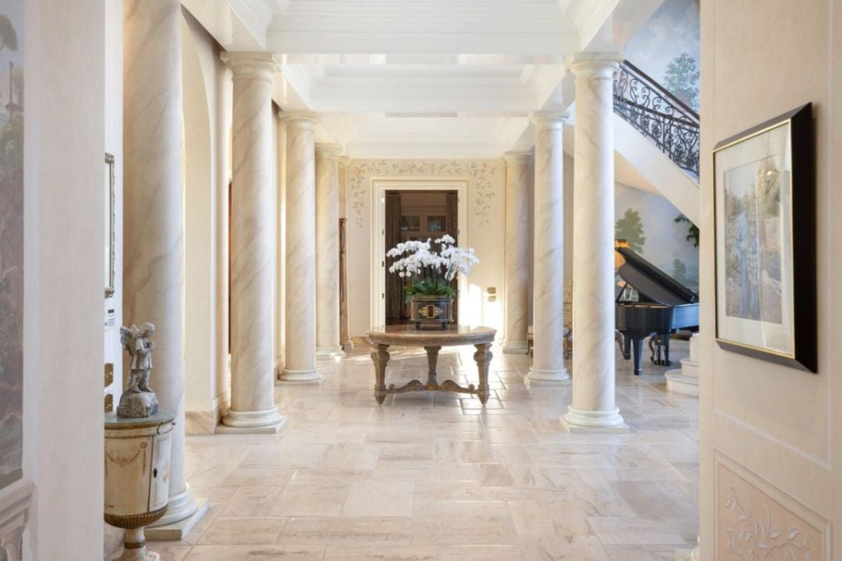 A foyer with a tiled floor, painting, and a center table with a vase on top.