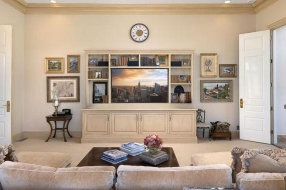 A living room with paintings, cabinets, shelves, TV, fireplace, couch, and center table.