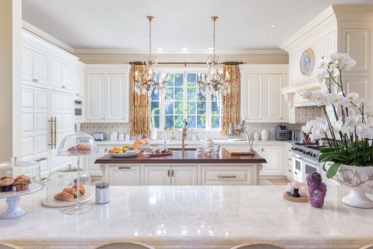 A kitchen with chandeliers, an island, countertops, sink, and cabinets.