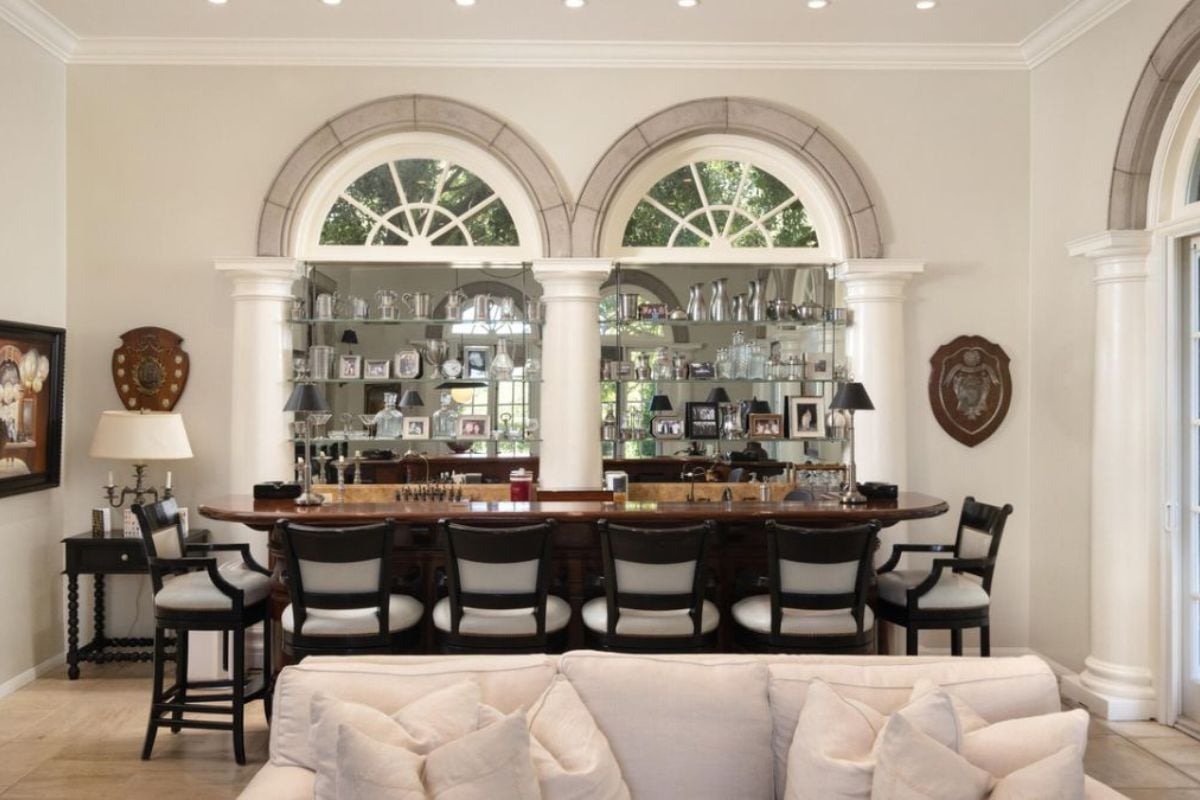 A bar with a painting, countertop, chairs, and wine rack.