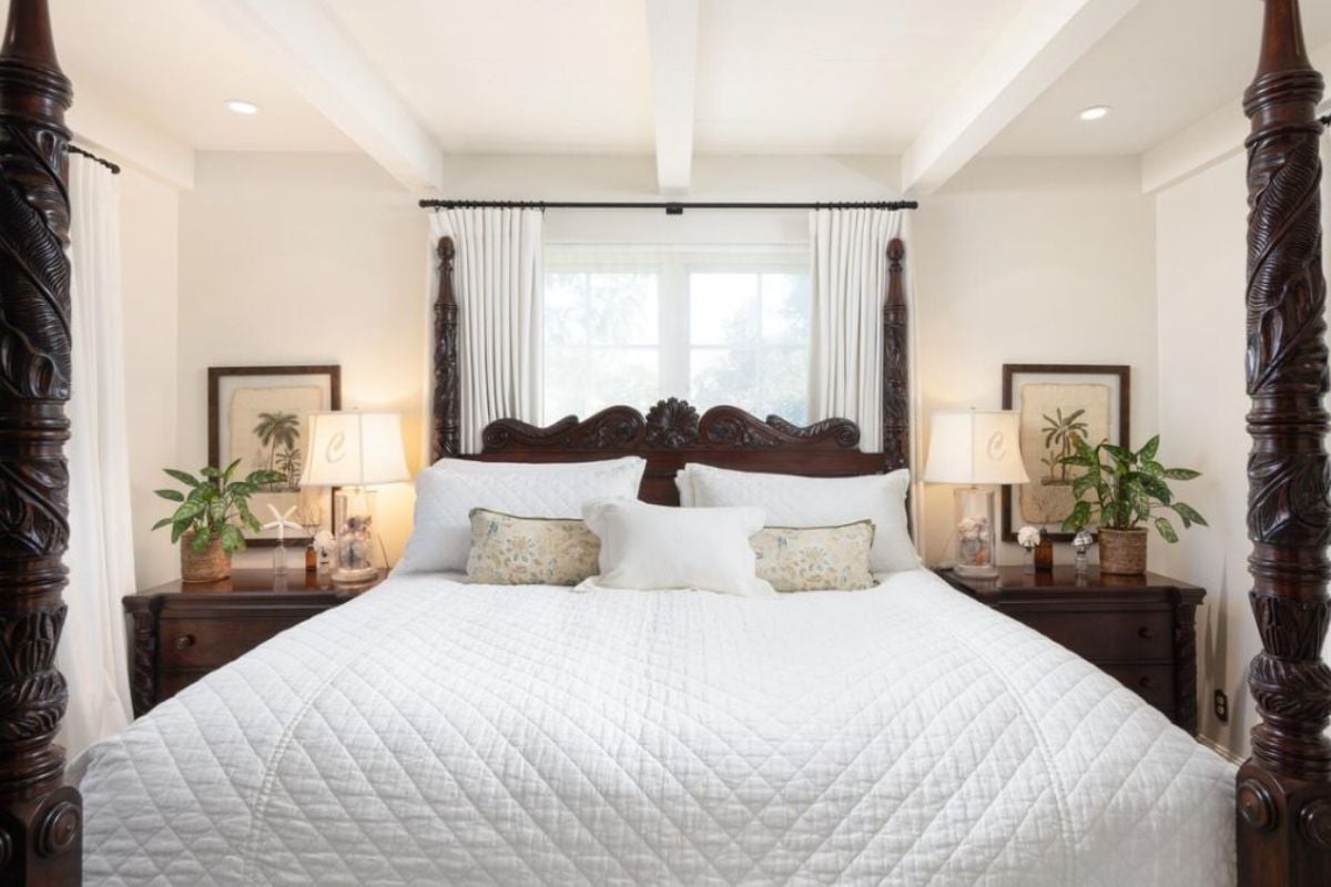 A bedroom with a canopy bed, nightstand, window, and lampshades.