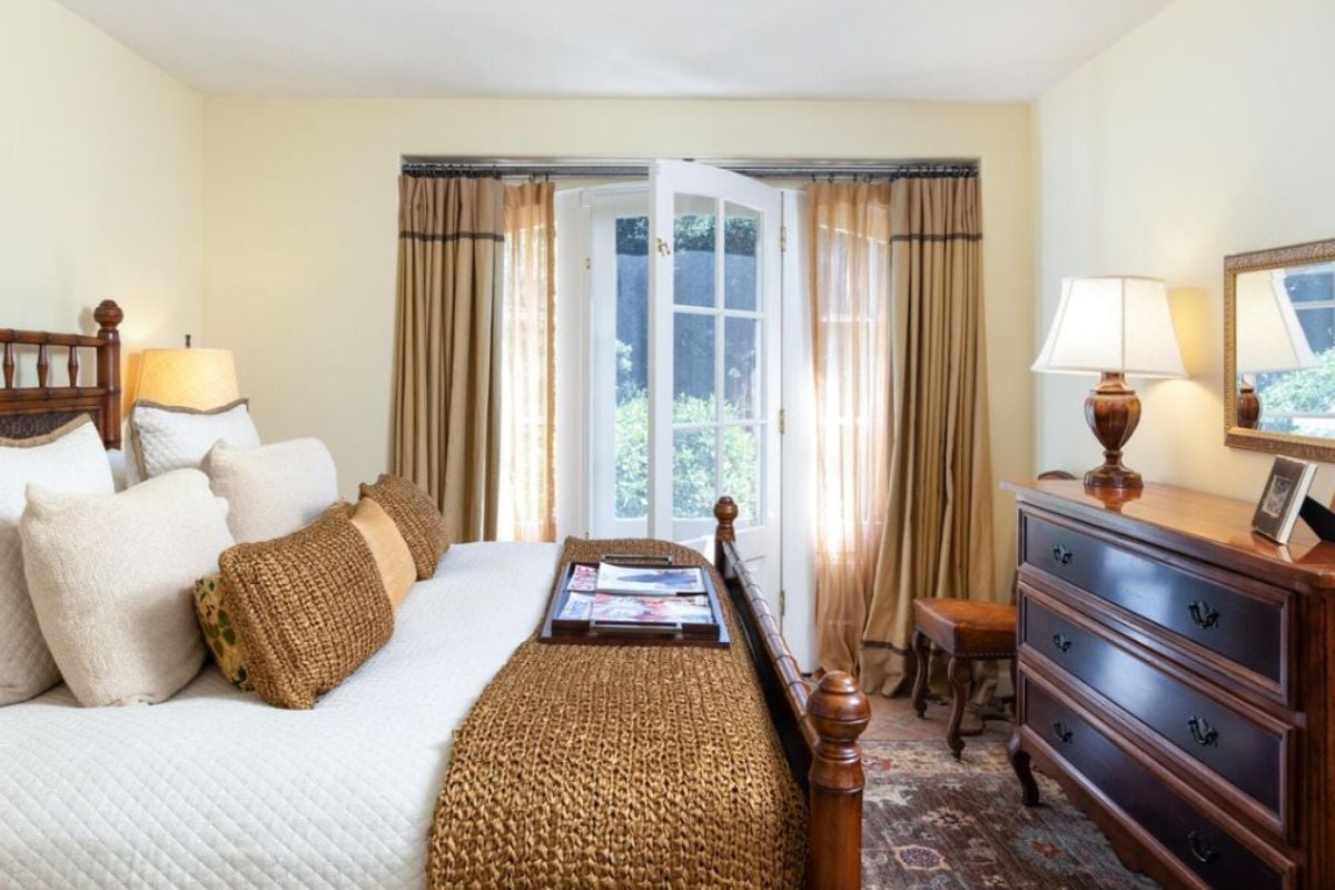 A bedroom with a bed, cabinet, mirror, and window.