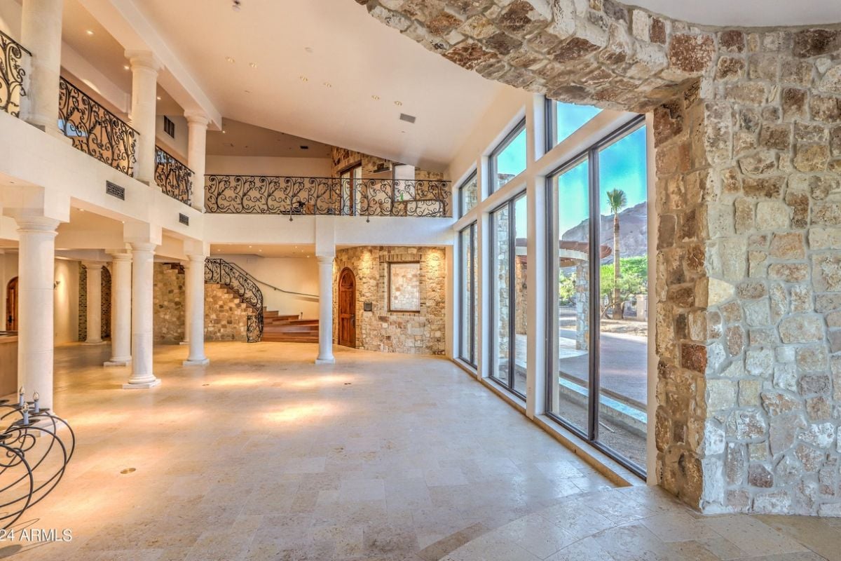 A foyer with a tiled floor, stone walls, staircase, and glass sliding doors.
