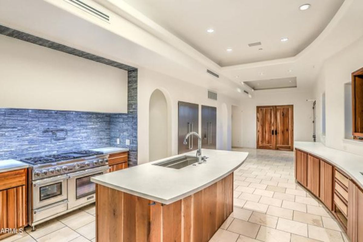 A kitchen with a tiled floor, center island, sink, cabinets, countertops, and kitchen appliances.