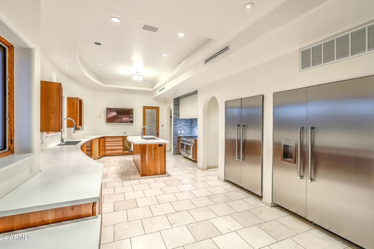 A kitchen with a tiled floor, center island, sink, cabinets, countertops, and kitchen appliances.
