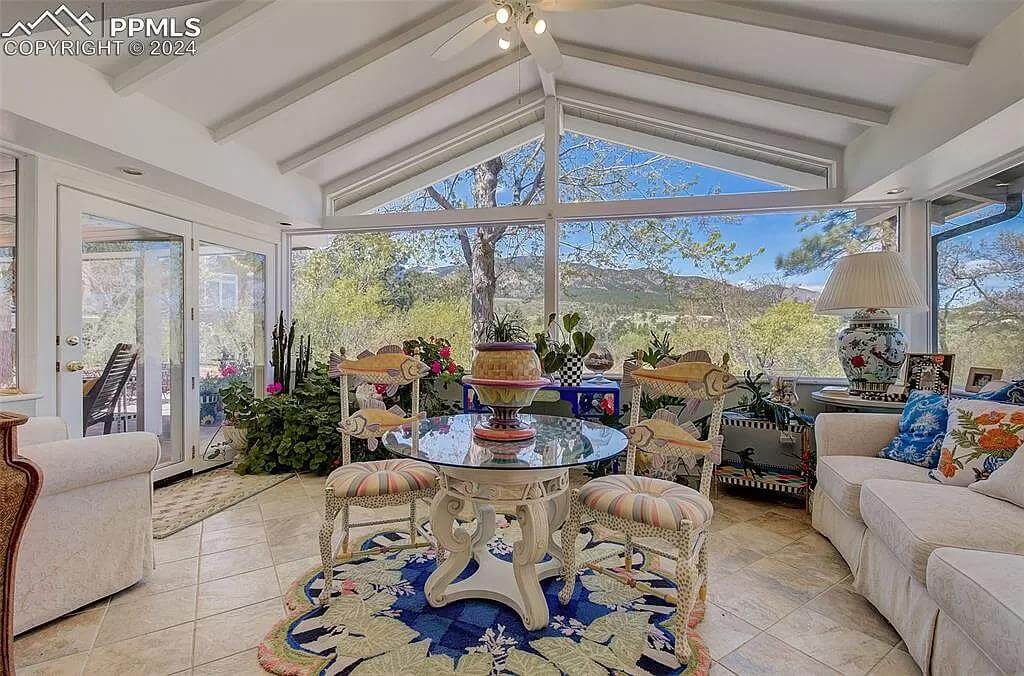 Sunroom with a round glass-top table, beige seats, and a vaulted ceiling with exposed beams.