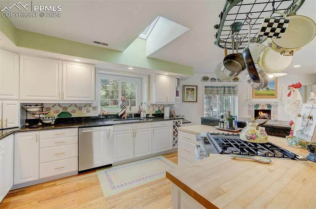 Kitchen with white cabinetry and a cooktop island topped by hanging pot rack.