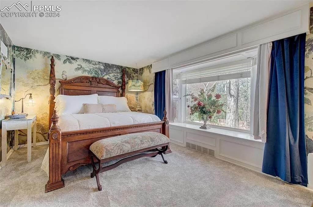 Primary bedroom with a wooden bed and a cushioned bench over the carpeted floor.