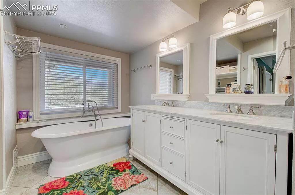 Primary bathroom with a dual sink vanity and a soaking tun under the louvered windows.
