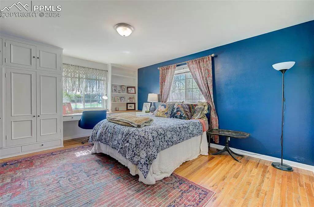 Bedroom with a blue accent, a skirted bed, and a built-in desk against the window.