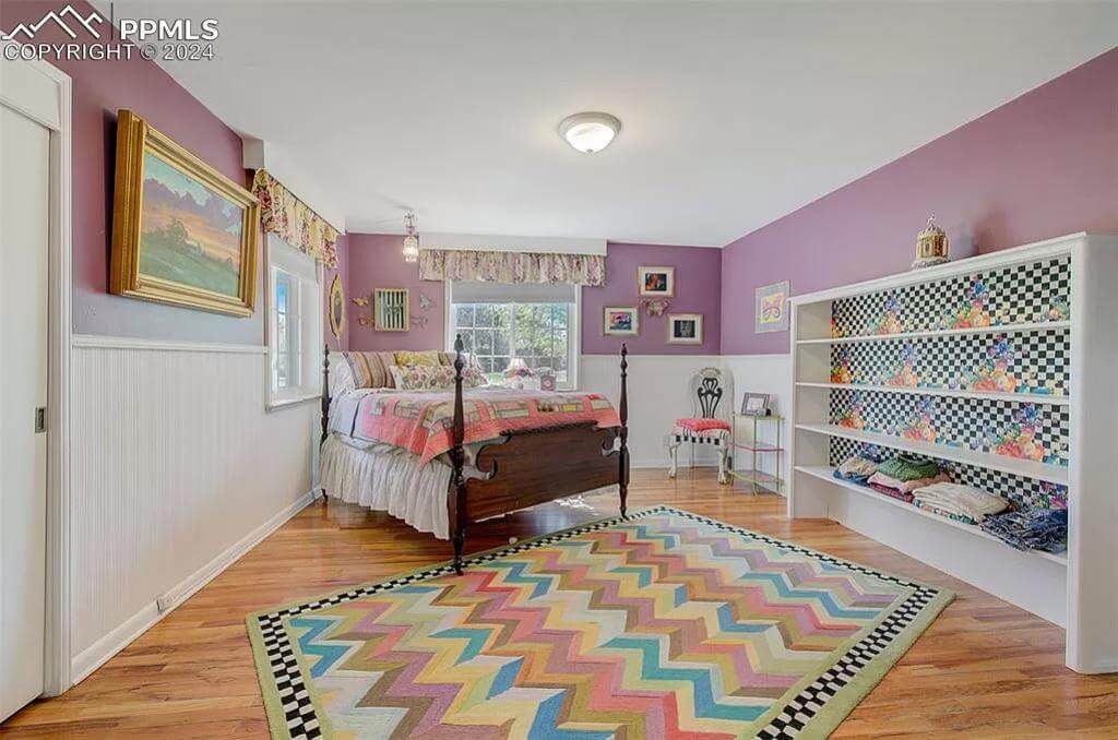 Bedroom with a four-poster bed and a colorful chevron rug over the hardwood flooring.