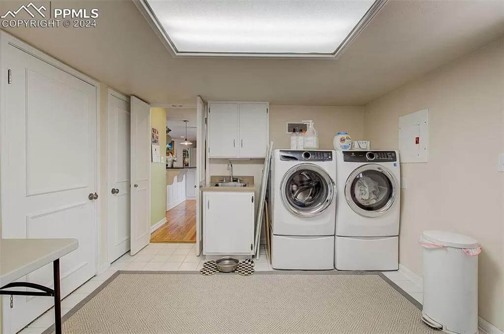 Laundry room with front-load appliances, white cabinets, and a utility sink.