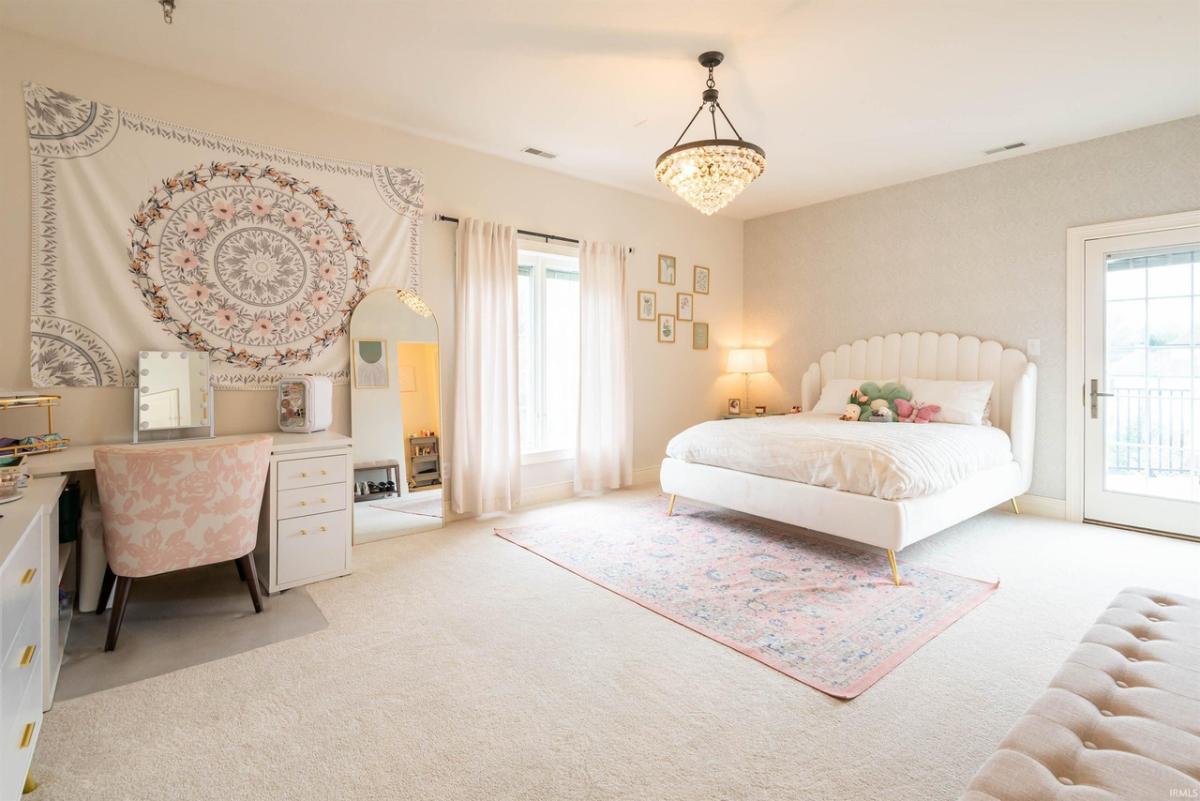 Bedroom with a large bed, chandelier and carpet flooring.