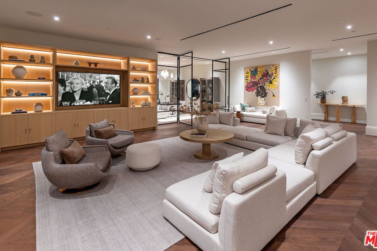 A living room with a TV, shelves, white couches, chairs, and coffee tables.