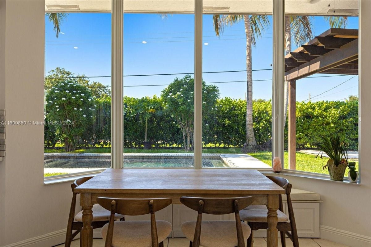 A dining room with windows and a table surrounded by chairs.
