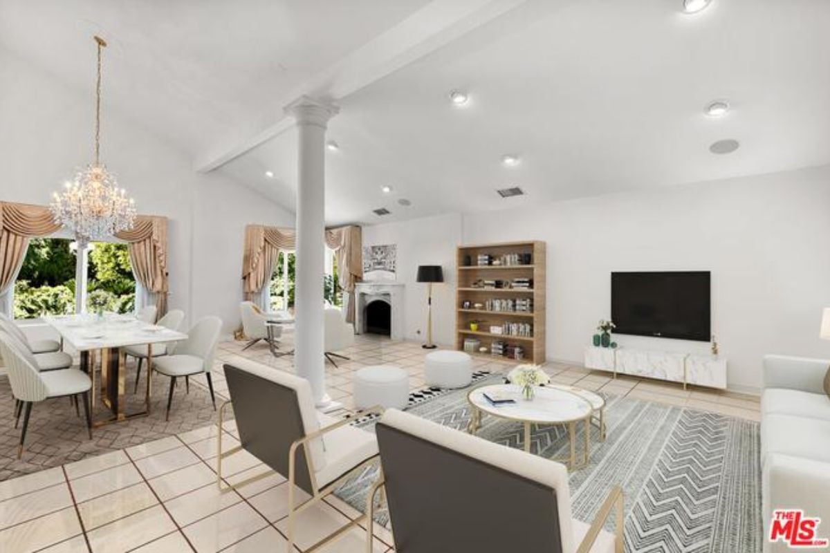 A living room with chairs, a TV, fireplace, tiled floor, chandelier, and a dining table surrounded by chairs.