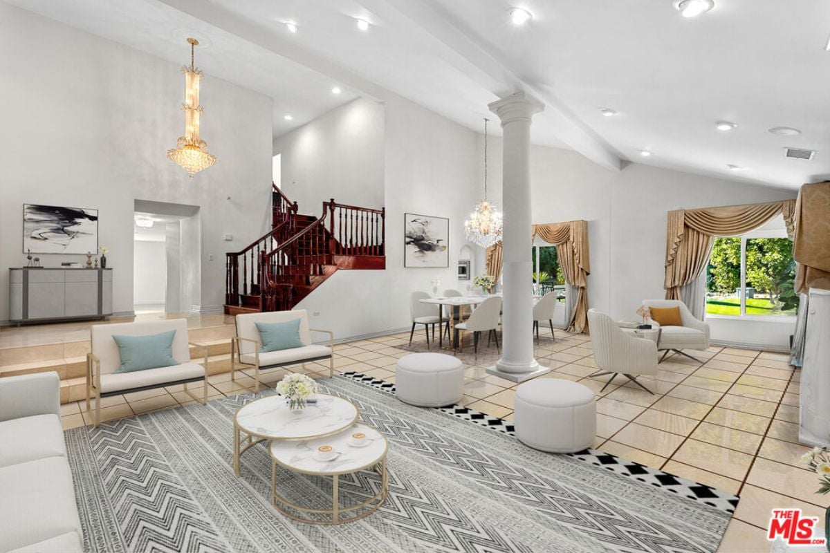 A living room with chairs, a TV, fireplace, tiled floor, chandelier, and a dining table surrounded by chairs.