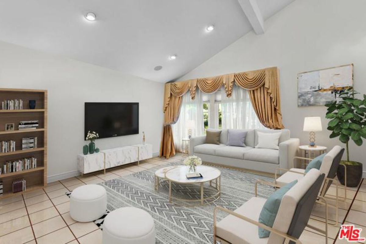 A living room with a TV, shelf, windows, couch, chairs, and a center table.
