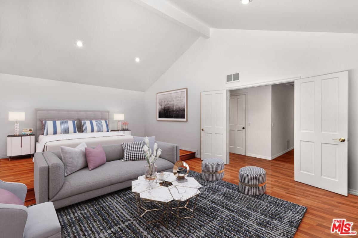 A bedroom with a bed, painting, vaulted ceiling, nightstands, rug, couch, and center table.