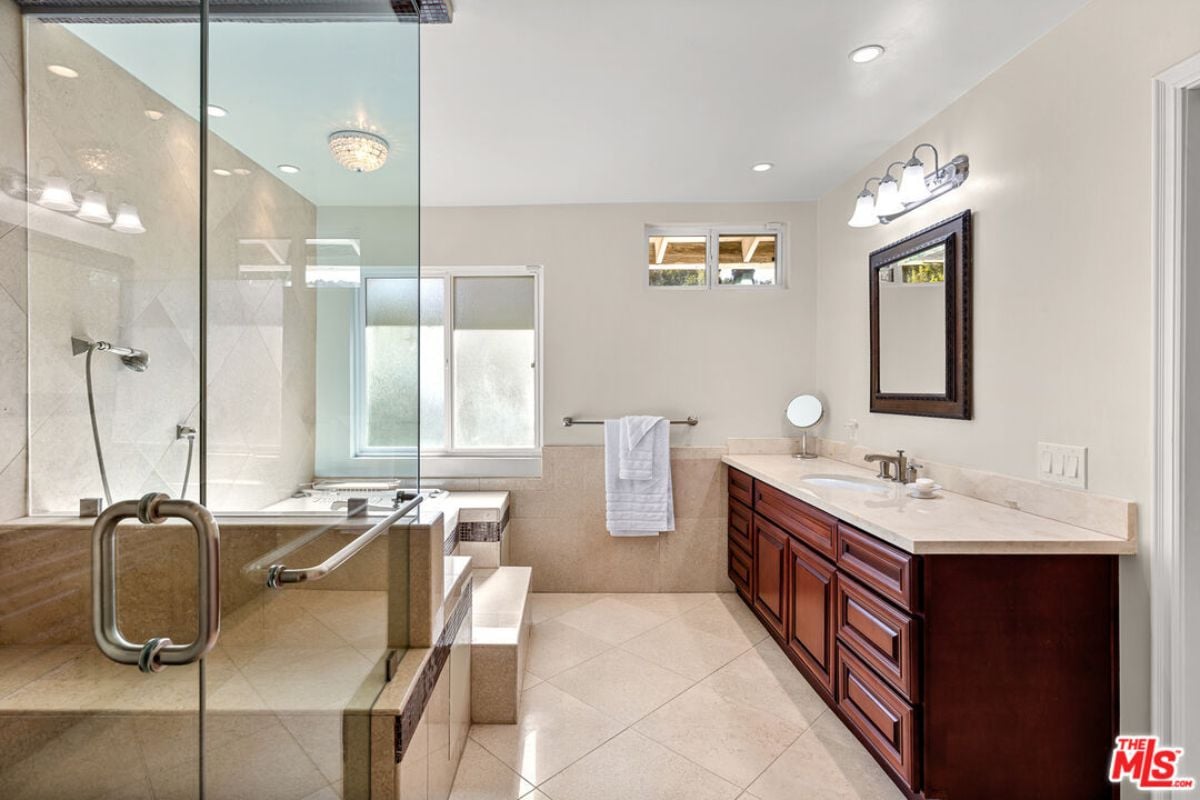 A bathroom with a tiled floor, countertop, cabinets, sink, and shower room.